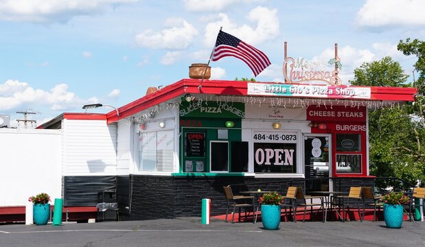 Gilbertsville, Pennsylvania, U.S.A - Jul 3 2026 - Little Gio's Pizza Shop with red roof, festive sign, menu boards, open sign, outdoor seating, and American flag.