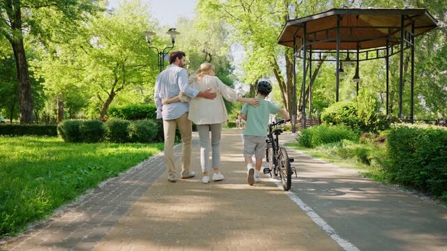 Family walks with son holding bike along sunny park path together