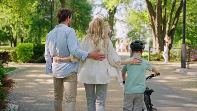 Family walks with bicycle held by son after lesson on park path