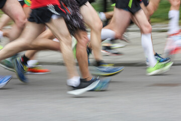 Naklejka premium Crowded marathon pack racing on asphalt with blurred legs and colorful running shoes. Close low angle captures speed, endurance and competitive momentum