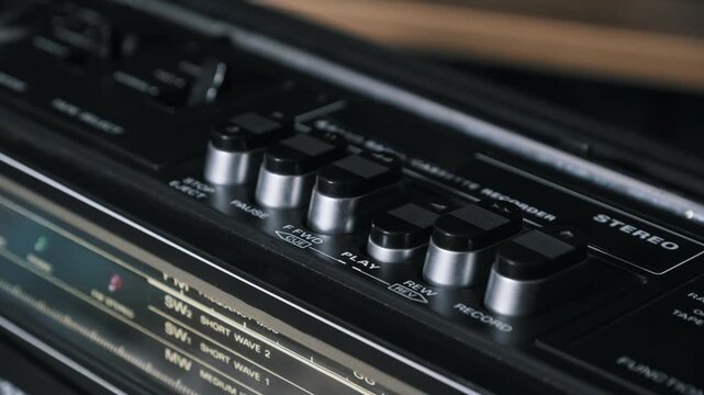 A male finger presses the play button on a black vintage cassette recorder to start music playback. Concept of listening to retro music, analog audio technology and nostalgia.