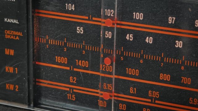 The indicator on a dusty, vintage analog radio tuner moves across the frequency scale, searching for a station. Concept of nostalgia, retro technology, communication, and searching for a signal