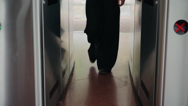 A person's legs walking through an automatic ticket gate at a subway or train station. The electronic barriers open to allow passage.