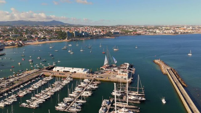 A drone rises above a marina revealing rows of yachts and sailboats along the docks