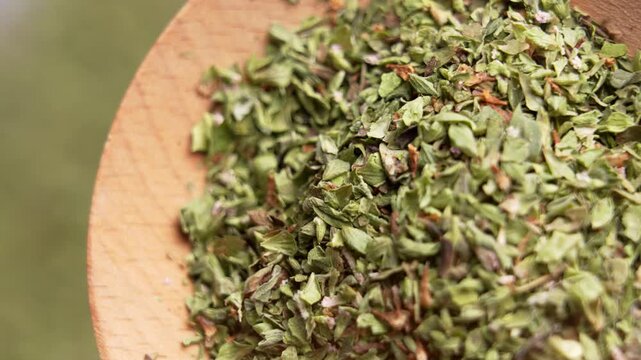 Macro view of dried oregano leaves filling a rustic wooden spoon