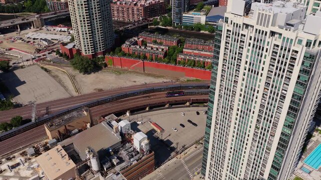 Elevated aerial tripod perspective showing train travelling on rail lines near skyscraper in downtown Chicago's Fulton River District on sunny day