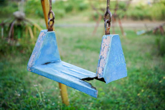 Broken plastic children's swing on the playground, old and unsafe swing. Old blue swing in an abandoned outdoor playground rustic environment