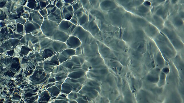 A top-down cinematic close-up shot of clear water ripples with bright sunlight caustics, creating shimmering light patterns and abstract textures on the swimming pool surface