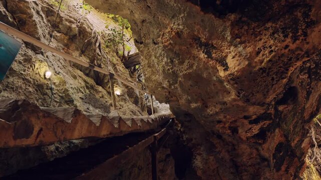 Close view of rugged natural rock formations surrounding a man-made staircase inside a coastal cave. Sunlight filters in from above, illuminating the geological textures.