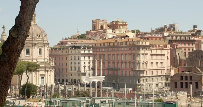 A scenic view of the rooftops of Rome, Italy, featuring the majestic dome of Santa Maria di Loreto on the left, historical palaces, terracotta-colored buildings, and ancient architectural ruins.