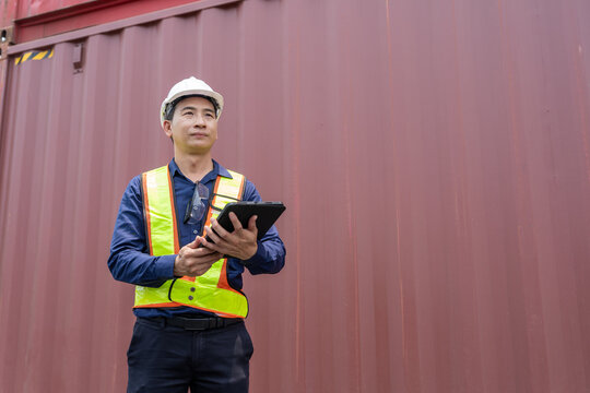 Logistics supervisor engineer using digital tablet inside container yard, Asian industry worker wearing hardhat and safety vest inspecting managing shipping import export delivery transport warehouse