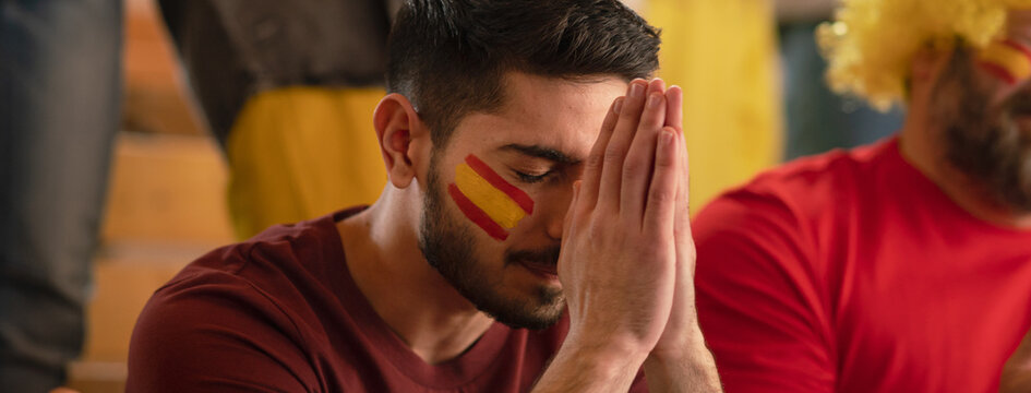 Sad football fan sitting at football stadium, spanish national team in live soccer match.