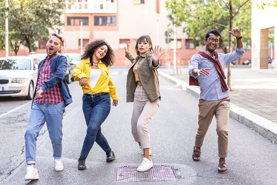 Energetic diverse friends dancing playfully on a quiet city street. Multiethnic millennials and gen z show carefree joy and movement outdoors. Urban youth concept