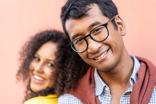 Smiling young man in glasses posing close to a friend against a coral wall. Selective focus portrait with warm tones and blurred background. Friendship concept