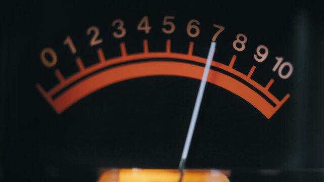 Macro shot of an analog VU meter with a needle fluctuating across an orange scale. It measures audio signal strength and volume levels on vintage sound equipment.