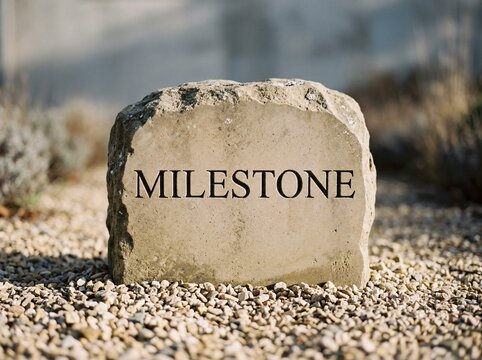 Carved stone milestone marker engraved with bold serif text standing on pale gravel in soft morning light