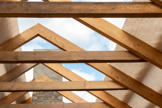 Wooden roof trusses and beams forming the framework of a new house, a significant phase in residential building construction, with blue sky visible through the unfinished structure