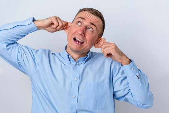 Adult Caucasian man in a blue shirt pulling both ears with hands and making a funny face, expressing humor and playful goofiness against a clean background