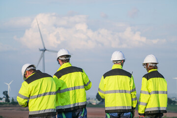Four wind energy engineers in matching yellow watch the rotors churn the evening sky overlooking the turbine studded plain in amber golden hour at a renewable energy site in Thailand. © ultramansk