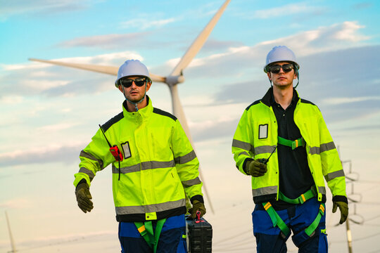 Two technicians with a tool case talk quietly on the dusk lit straight on an empty rural road through the park in hazy sunset light on a working wind farm in rural Thailand image 6508.