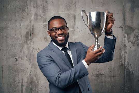 Successful african american businessman holding a silver trophy cup, smiling at the camera, professional achievement and career success concept