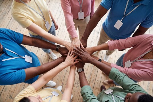Diverse group of people putting their hands together in a circle, showing unity, teamwork, and collaboration in a professional or volunteer setting