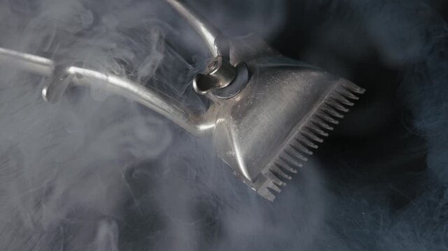 Vintage manual hair clipper lies on a dark, reflective surface. Ethereal white smoke slowly billows and swirls around the classic barber tool, creating a mysterious atmosphere.