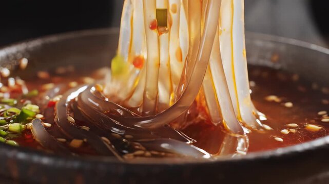 Chopsticks lifting translucent glass noodles from spicy Sichuan chili oil soup in a steaming bowl