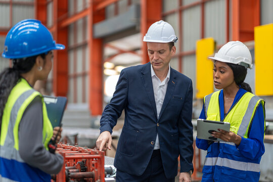 multiethnic group of industrial engineers and inspector wearing safety vests and hard hats working together in a manufacturing facility