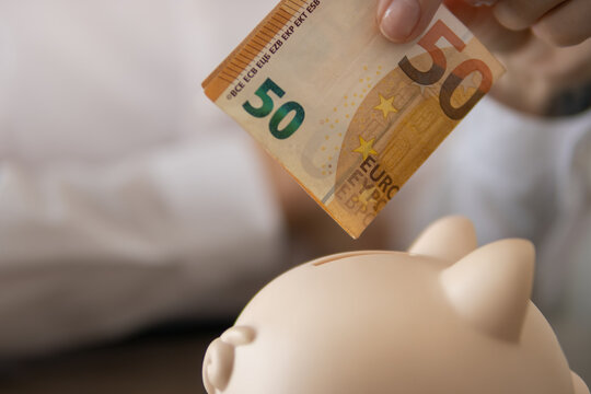 Hand placing fifty euro banknote into a pink piggy bank, representing financial savings, budget management, deposit, investment, future wealth, and economic stability