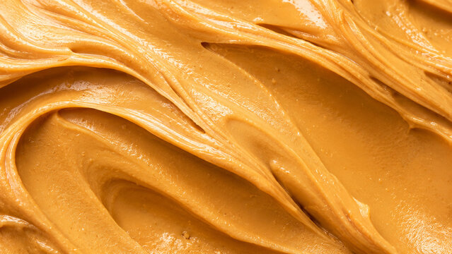 Creamy peanut butter swirl texture with smooth glossy surface in a macro food background.