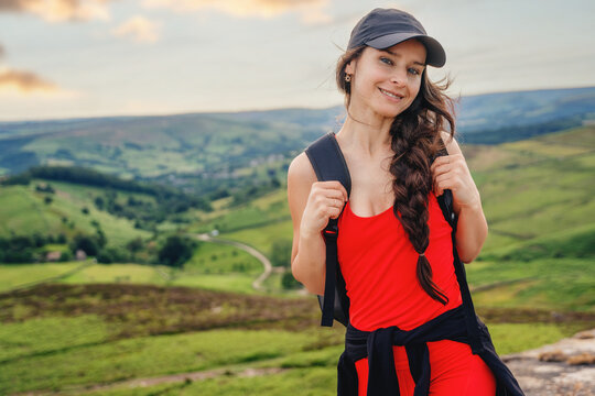 Woman stands on a hill smiling during a hike in a green landscape with hills and valleys in the background near sunset