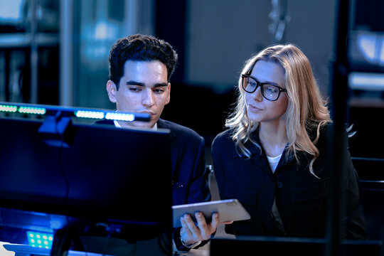 Monitoring AI training progress. Specialists oversee a machine learning model's training observing real time metrics on screen discussing adjustments via tablet interface late night.