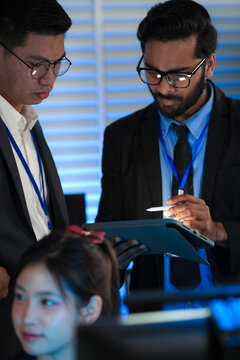 AI research team huddles late night innovators review complex machine learning model architecture discuss training data using tablet stylus futuristic lab code screens glow bright.