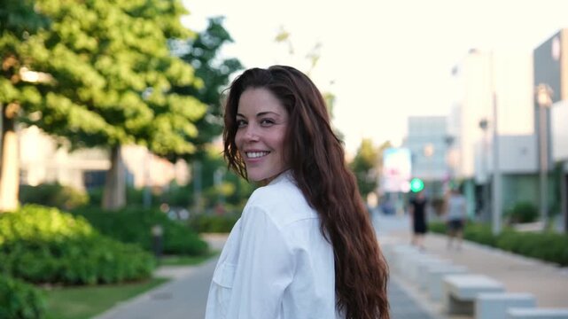 Charming young woman with long hair walking down a city street and smiling at the camera