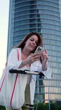Beautiful woman leaning on an electric scooter while using her smartphone in a modern city