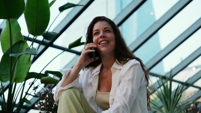Attractive young woman having a pleasant phone conversation while sitting in a modern space