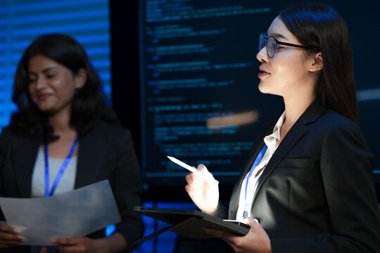 A female tech leader, an Asian woman, presents a new digital transformation strategy using a tablet. Her diverse team discusses sustainable AI solutions for future growth.