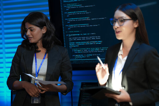 An Indian female developer leads a code review, holding a report. She explains a Python script for an AI or cybersecurity system to her team in a dark SOC Security Operations Center.