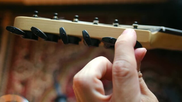 Close up musician hands turning tuning pegs on headstock of electric guitar to adjust pitch of strings, preparing for performance or practice session. Musician tuning an electric guitar headstock