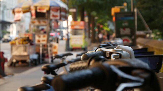 Manhattan Midtown street New York City, United States. Rental bicycle parking, Central Park West summer trees greenery. Bike for rent in row. People pedestrian on sidewalk pavement. Hot dog fast food.