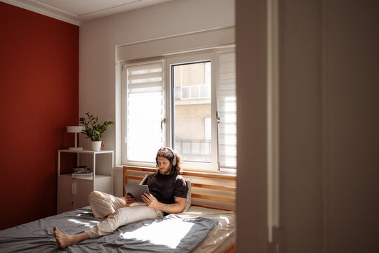 Man on Bed Using Tablet and Headphones