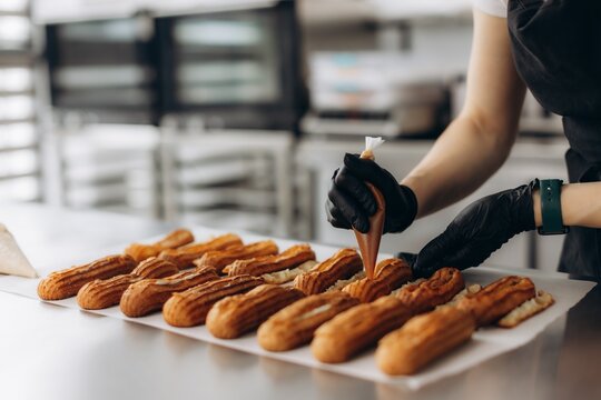 Pastry chef decorating eclairs with chocolate cream