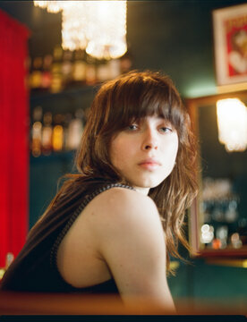 Young woman sits at a bar looking back with a thoughtful expression