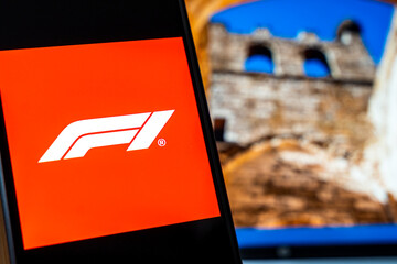 Obraz premium Warsaw, Poland - July 6, 2026: Close-up of an F1 logo displayed on a smartphone screen with a blurred background of a historical site, representing the world of motorsport and technology.