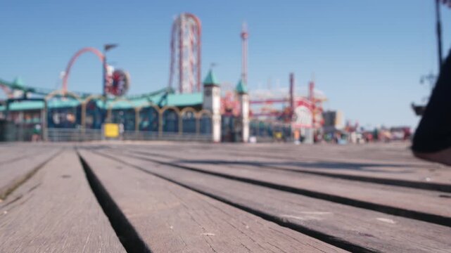 Coney Island beach promenade in Brooklyn, New York, United States. Wooden boardwalk near retro luna park. Amusement park on ocean coast beach. Waterfront summer holiday, people walking on promenade.