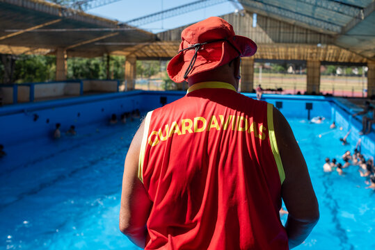Back View of Lifeguard in Red Uniform Watching Over Swimmers at Swimming Pool