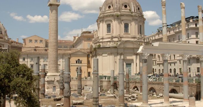 A magnificent closeup of Trajan's Column standing next to the Church of the Most Holy Name of Mary at the Trajan Forum in Rome, Italy, captured beneath a beautiful, bright blue sky with clouds.