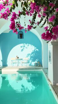 Santorini island, Greece. White cycladic architecture and luxury swimming pool with blue water. Pink flowers over the pool. Travel and vacation concept. Vertical video
