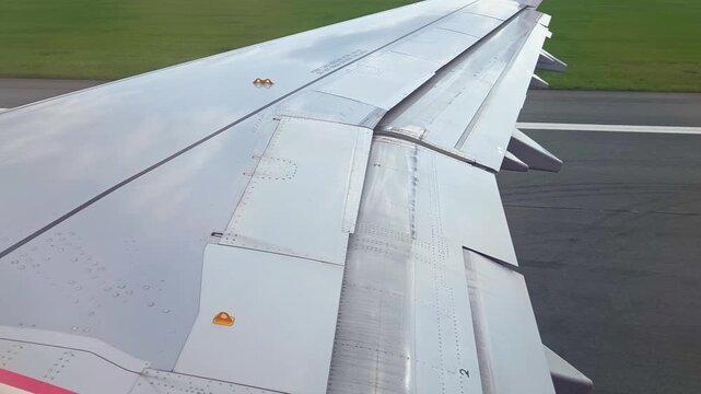 Aircraft wing view showing flaps in motion during landing approach, highlighting aerodynamic components and runway markings in the background